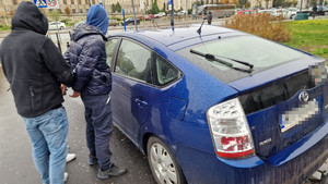 policjant zakłada kajdanki mężczyźnie przy taksówce