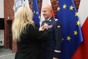 Kobieta stoi tyłem i przypina odznaczenie Komendantowi Głównemu Policji