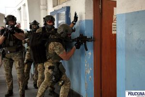 Czterech kontrterrorystów stoi za ścianą przy drzwiach, pierwszy zagląda za drzwi do pomieszczenia