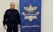 Umundurowany Policjant na tle logo Komendy Miejskiej Policji w Skierniewicach