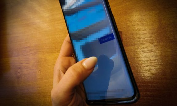 Kobieca dłoń trzyma telefon, na którym jest włączona aplikacja do logowania