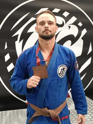 Młodszy aspirant Karol Kurembski w stroju do Jiu Jitsu prezentuje medal zawieszony na szyi