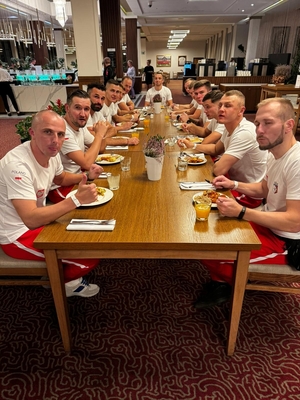 zawodnicy w trakcie posiłku na stołówce siedzą przy długim stole naprzeciwko siebie