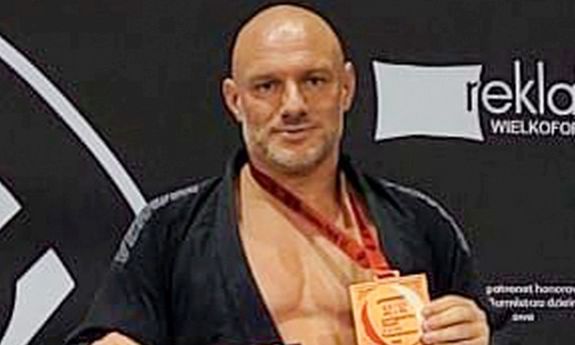 Mężczyzna w czarnym stroju stoi na podium i ma na szyi medal na czerwonym pasku