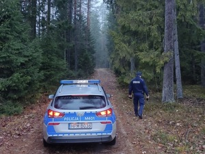 radiowóz zaparkowany na leśnej drodze, obok stoi umundurowany policjant