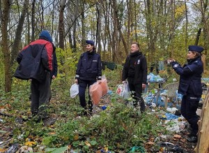 Teren zalesiony. Dwie policjantki i wolontariusz stoją naprzeciwko osoby bezdomnej