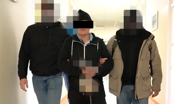 dwaj funkcjonariusze prowadzą zatrzymanego korytarzem