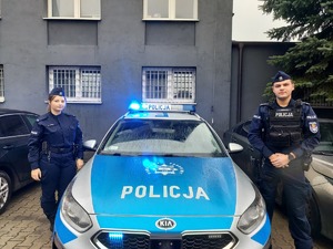 policjant i policjantka stoją przy radiowozie policyjnym
