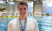 zdjęcie przedstawia mężczyznę pozującego do zdjęcia z medalami, w tle widoczny basen