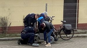 Zdjęcie z monitoringu. Policjanci pomagają mężczyźnie, któremu uszkodziło się koło przy wózku inwalidzkim
