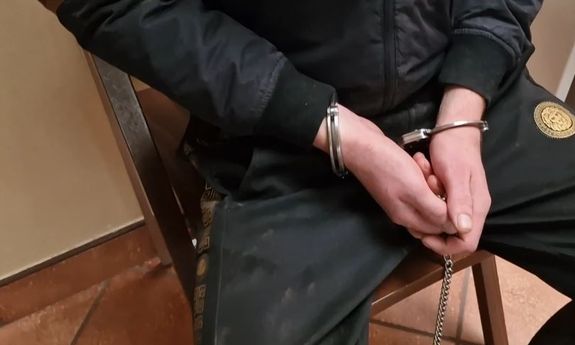Na krześle siedzi mężczyzna skuty kajdankami