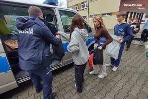 policjant przy radiowozie pakuje dary, które przynosi młodzież szkolna