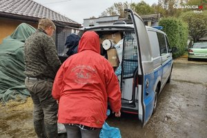 policjant i dwie osoby stoją przy radiowozie wypełnionym darami dla zwierząt