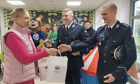 Dwaj policjanci wręczają przedstawiciele hospicjum podarunki