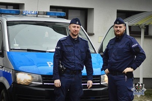 Na tle oznakowanego radiowozu stoi dwóch policjantów