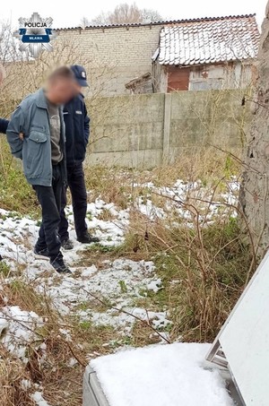 policjant z zatrzymanym mężczyzną na jego posesji