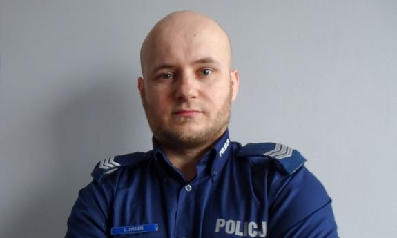 Policjant stoi na tle szarej ściany