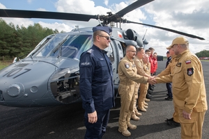 policyjni lotnicy i strażacy stoją przy policyjnym śmigłowcu