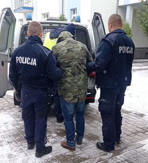 trzech policjantów prowadzi zatrzymanego mężczyznę do radiowozu