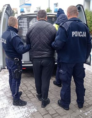 trzech policjantów prowadzi zatrzymanego mężczyznę do radiowozu