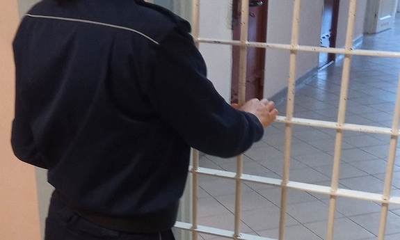 Umundurowany policjant zamykający kraty do policyjnego aresztu. W tle widoczne drzwi do poszczególnych cel