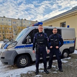 Dwóch umundurowanych policjantów stoi na tle oznakowanego radiowozu