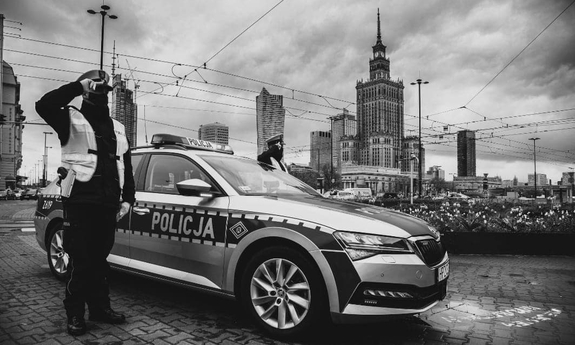 Zdjęcie czarno-białe. Policjant stoi przy radiowozie policyjnym