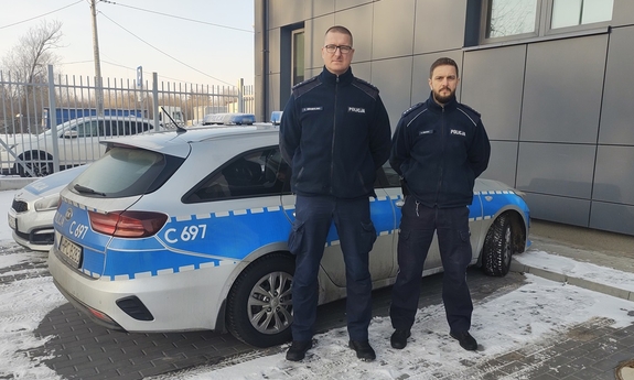 dwaj policjanci stoją przed radiowozem