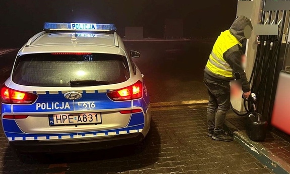 Mężczyzna nalewający paliwa do kanistra obok zaparkowanego radiowozu