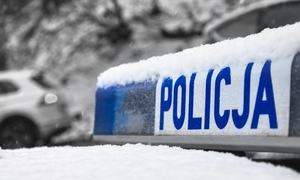 Przyprószony śniegiem sygnalizator świetlny na dachu radiowozu policyjnego z napisem Policjia