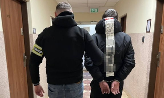 policjant prowadzi korytarzem zatrzymanego zakutego w kajdanki