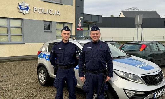 dwóch umundurowanych policjantów stoi przy radiowozie