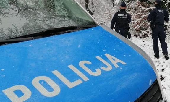 Maska radiowozu z napisem policja i w tle dwóch policjantów. Sceneria śnieżna