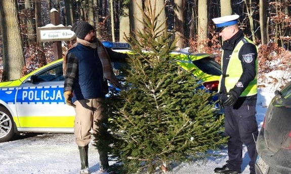 policjant i mężczyzna trzymający choinkę, za nimi stoi radiowóz policyjny