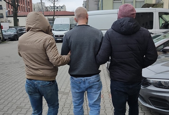 dwóch policjantów prowadzi zatrzymanego mężczyznę