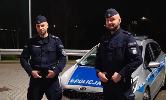 dwaj policjanci stoją przy radiowozie