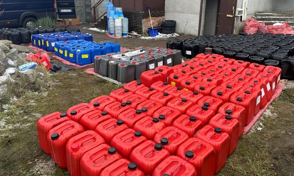 na posesji przed budynkiem stoją plastikowe pojemniki w kolorach czarnym, szarym, niebieskim i czerwonym, w tle widoczna część samochodu typu bus