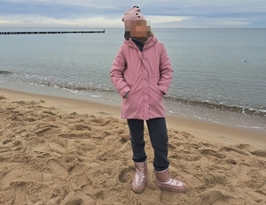 dziewczynka w różowej czapce na głowie i różowej kurtce stoi na plaży