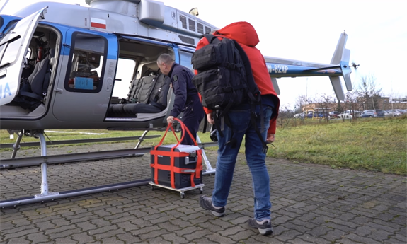 Dwaj mężczyźni wnoszą pojemnik do transportu organów na pokład policyjnego śmigłowca.