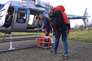 Dwaj mężczyźni wnoszą pojemnik do transportu organów na pokład policyjnego śmigłowca.