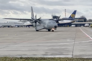 Dwusilnikowy samolot kołuje na płycie lotniska. W tle stoi samolot pasażerski.