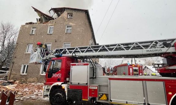 Pojazd straży pożarnej. W tle budynek po wybuchu i bez dachu