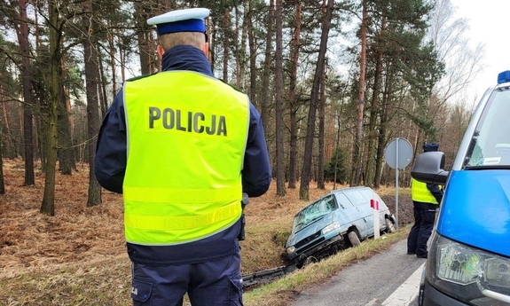 umundurowany policjant, radiowóz i samochód w rowie