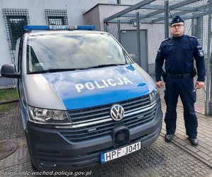 Obok radiowozu stoi policjant