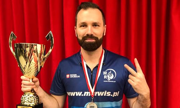 Policjant stoi na czerwonym tle i trzyma w ręku puchar