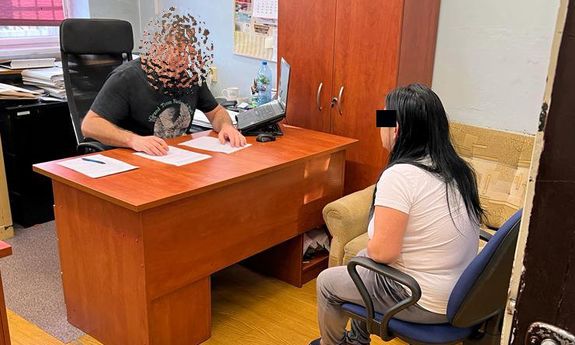 W pokoju przy biurku siedzi policjant i zatrzymana