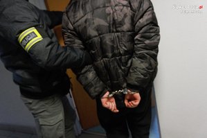 policjant prowadzi zatrzymanego mężczyznę w kajdankach