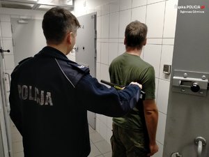 Zatrzymany Mężczyzna stojący tyłem, przeszukiwany przez umundurowanego policjanta detektorem do metalu