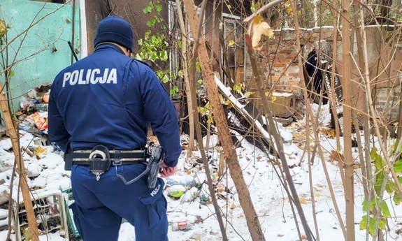 policjant w trakcie poszukiwań przy starym, opuszczonym budynku wśród zarośli