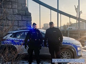 dwaj policjantów stoi przed radiowozem
